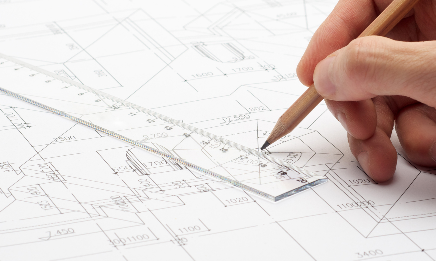 engineering sketch with clear 12 inch plastic ruler, hand holding a pencil, and a blueprint type part drawing on the table