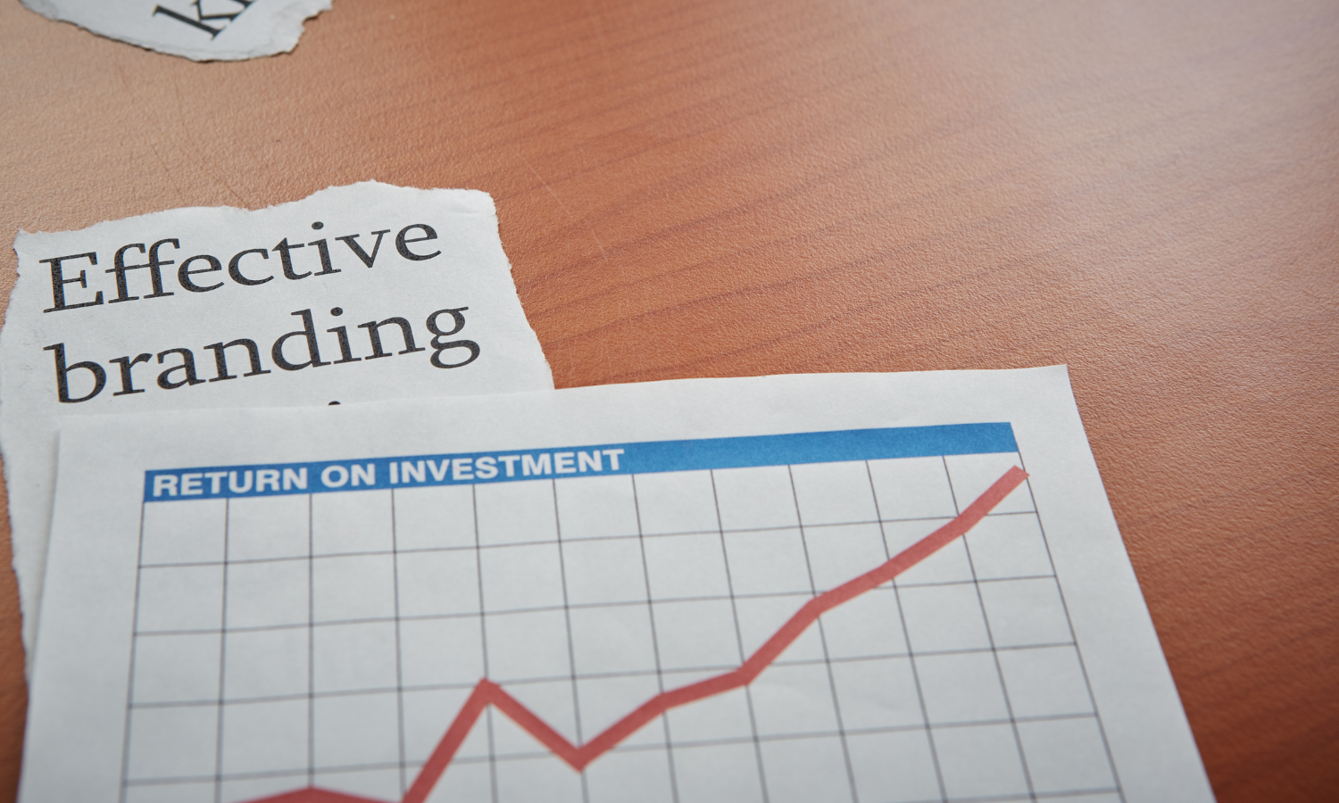 newspaper clipping with the headline:  Effective Branding and laid on top is another sheet of paper with a line graph showing upward trajectory labeled ROI
