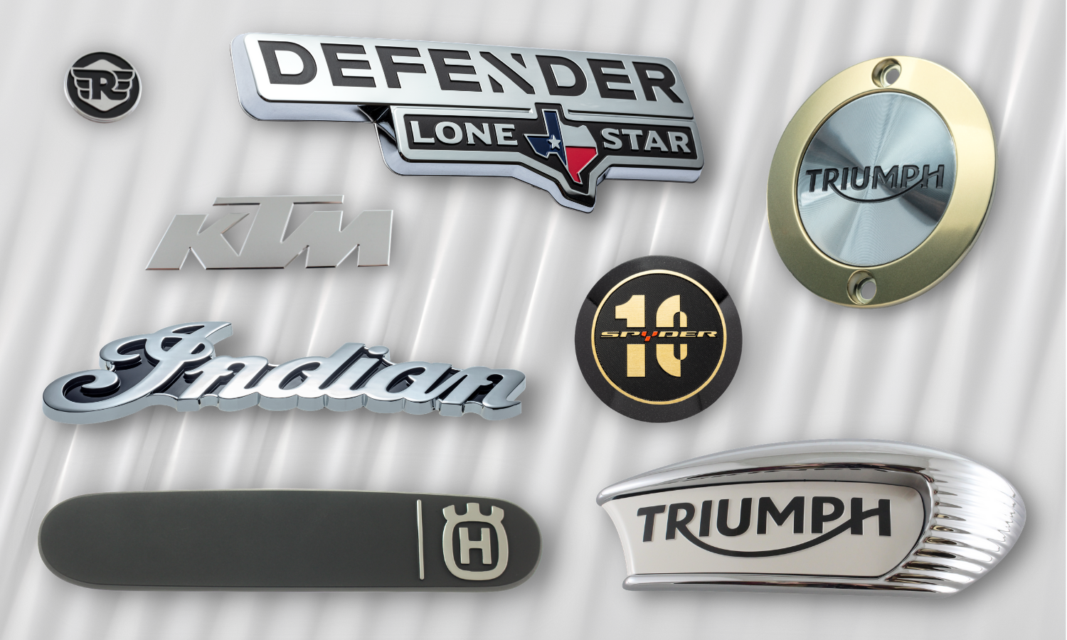 collage of parts that go on motorcycles; circle and oblong triumph motorcycle badges, chrome and black indian script badge, circle 10th anniversary black and gold spyder badge, chrome KTM badge, brushed black and chrome husqvarna trim badge, chrome and black defender lone star badge