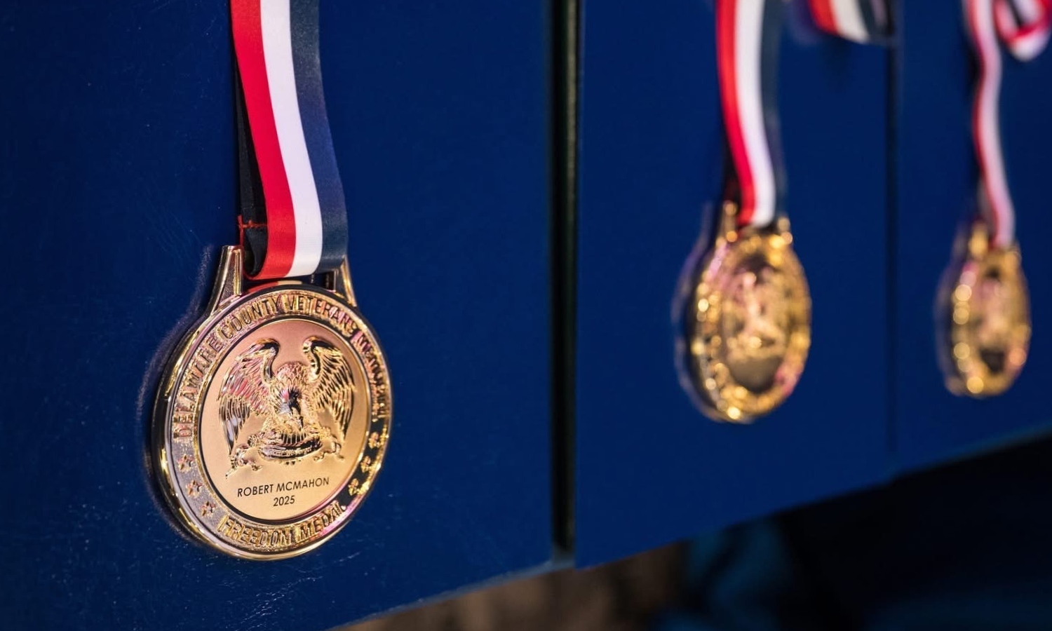 gold medals hung with red, white, and blue stripped ribbon hanging over a table with a navy blue table cloth.