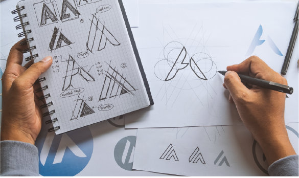 A hand sketching a logo shaped like an A using drafting paper and a pencil